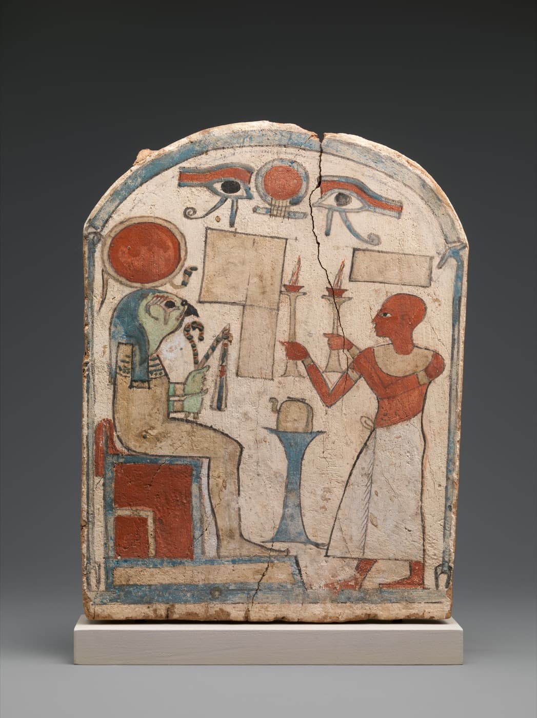 Painted wooden stela: a falcon-headed deity with a red solar disk sits opposite a man making an offering.