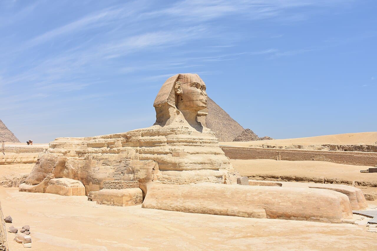 The Great Sphinx of Giza seen from the side, with a pyramid behind it